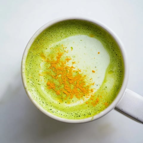 Steaming mug of Coconut Ginger Matcha Latte, vibrant green with a dusting of matcha and frothy coconut milk.