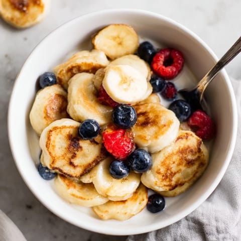 Delicious bite-sized pancakes topped with fresh berries, served with milk for breakfast.  