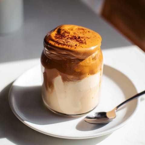 A close-up of a layered brown sugar dalgona latte with whipped coffee topping and ice.
