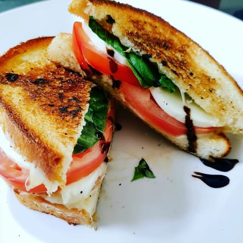 Perfectly grilled Caprese Salad Grilled Cheese showcasing melted mozzarella, drizzled balsamic, and fresh basil leaves.