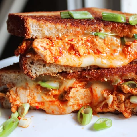 A close-up of a perfectly grilled Gochujang Mayo Chicken Sandwich: crispy bread and melted cheese pull.
