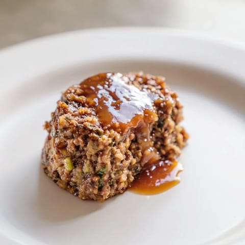 A close-up of tender, juicy mini meatloaf bites arranged on a plate with glistening sauce.