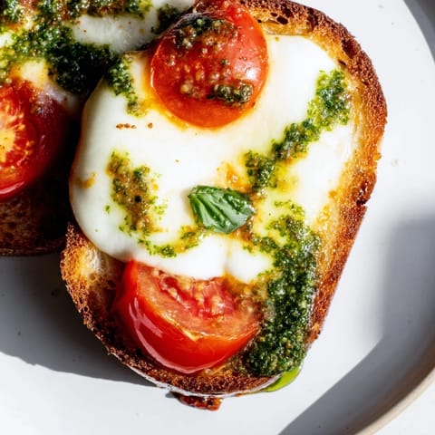 A close-up of a Caprese Pesto Grilled Cheese cut in half, showing gooey cheese and vibrant red tomatoes on fresh basil.  