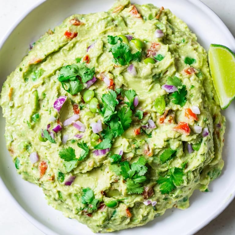 This vibrant bowl of fresh edamame guacamole features diced tomatoes and a generous cilantro garnish.