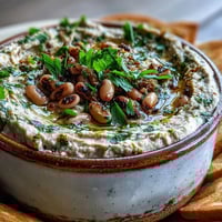 A creamy bowl of Smashed Black-Eyed Peas topped with olive oil and fresh parsley, perfect for dipping with pita chips.